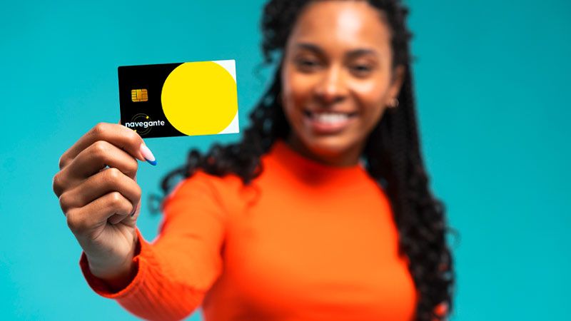 Jovem com cabelos compridos, camisola laranja e tez escura a sorrir, segura um cartão navegante em grande plano